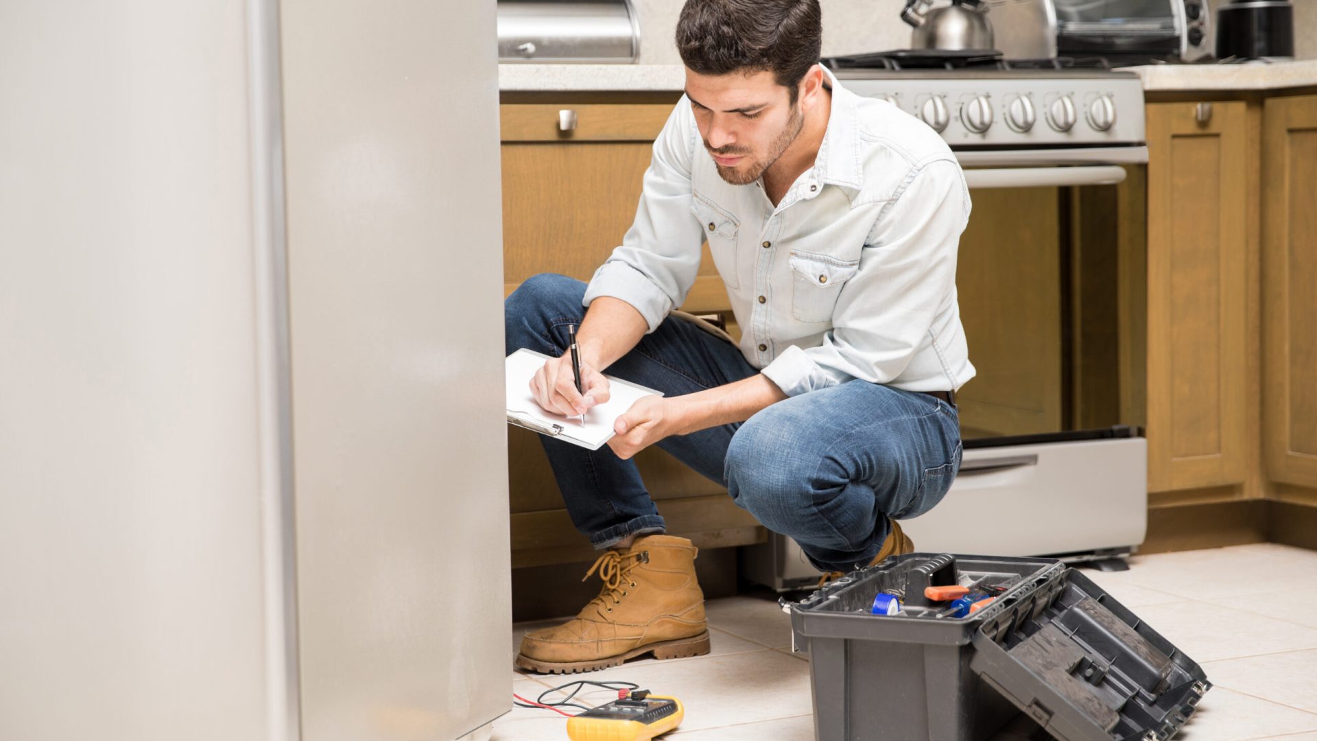 Portrait of a handsome male technician doing a work report on a broken fridge in a home kitchen